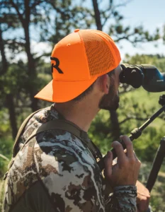 Hunter using his scope wearing a blaze orange custom Richardson hat with a black embroidered logo
